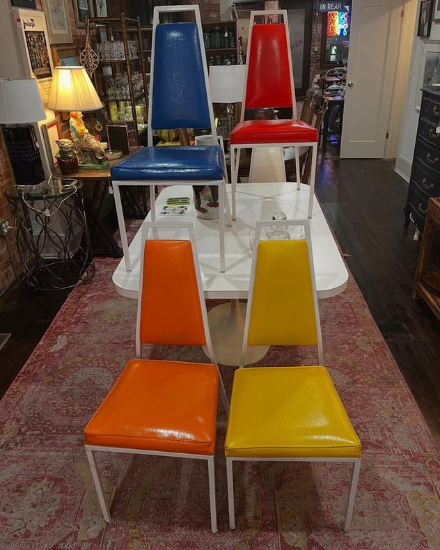 Mid century white laminate tulip style dining table with 6 multicolored chairs! Table is 60” x 40” x 29” Chairs are 17.5” x 22” x 41” seat height 19” small tear to corner of green chair and orange chairs 