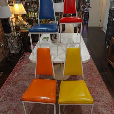 Mid century white laminate tulip style dining table with 6 multicolored chairs! Table is 60” x 40” x 29” Chairs are 17.5” x 22” x 41” seat height 19” small tear to corner of green chair and orange chairs 